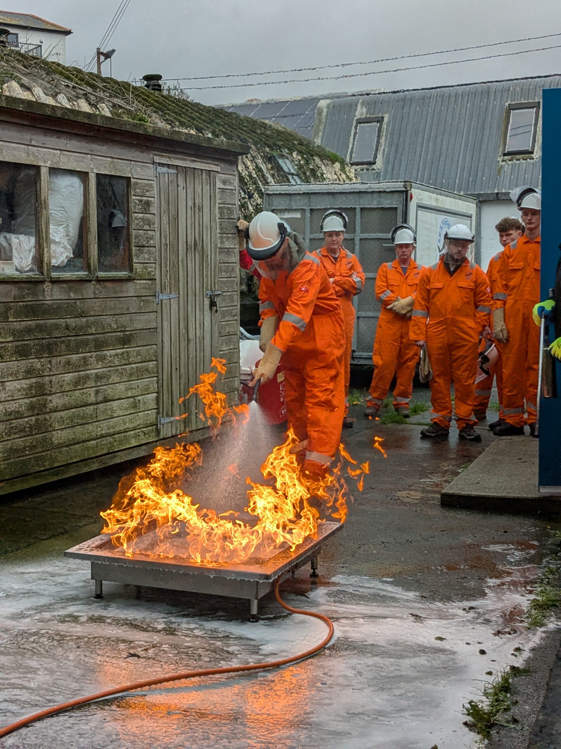 Students on a fire fighting course wearing protective clothing extinguishing a fire